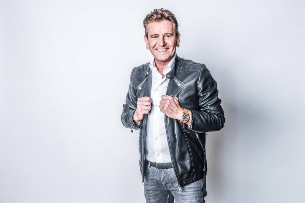 Luc Steeno tijdens een live optreden, zingend voor een enthousiast publiek met een warme en stijlvolle uitstraling