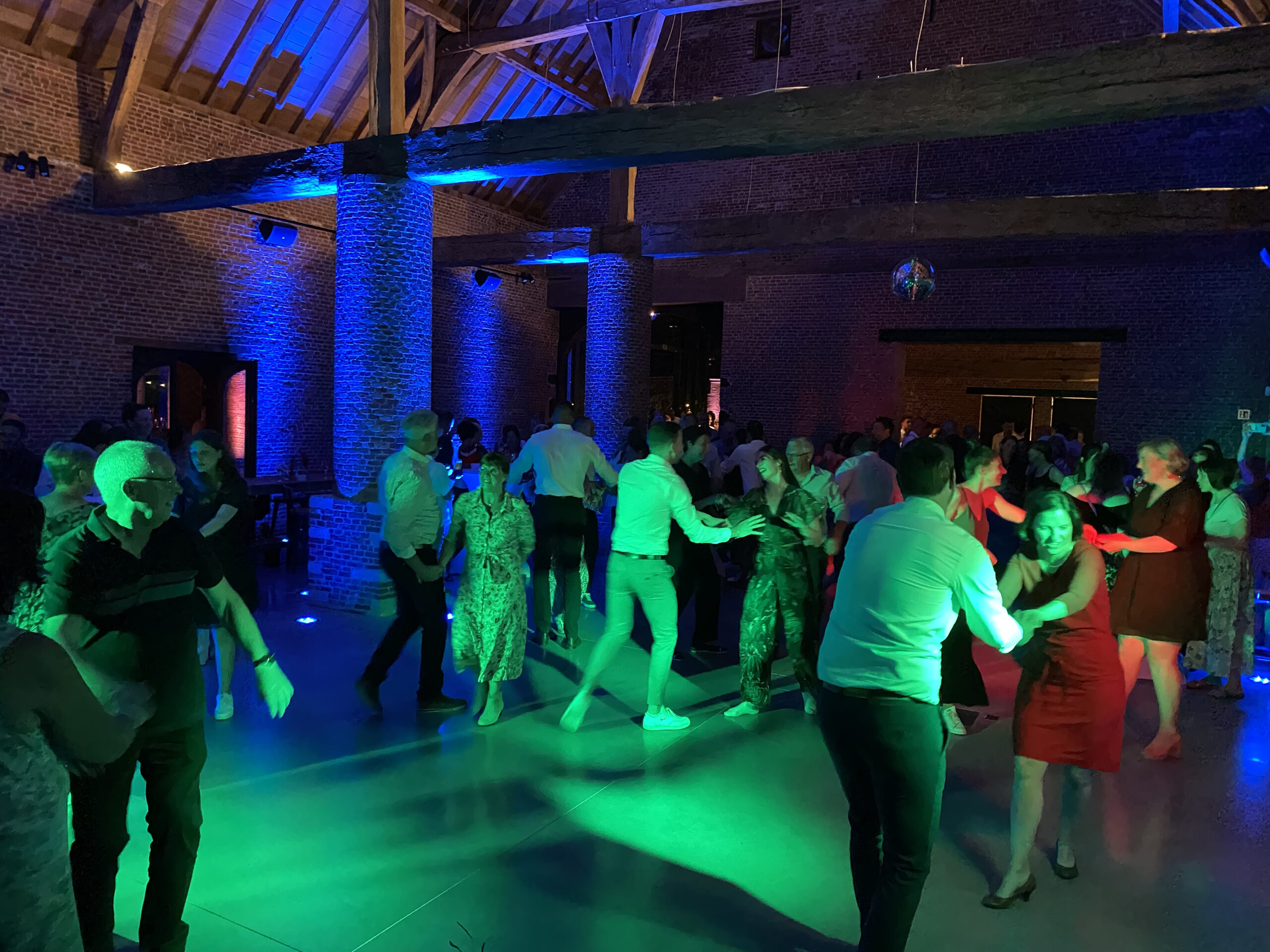 Professionele DJ achter discobar met sfeerverlichting en dansende gasten tijdens een privéfeest.