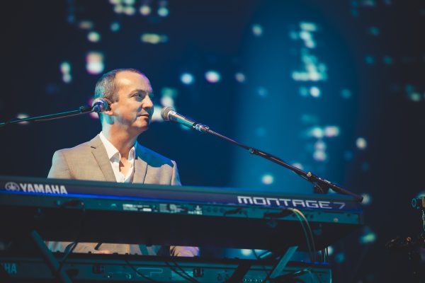 De Miguel Wiels Band live op het podium tijdens een concert, met muzikanten in actie en een sfeervol verlicht decor.